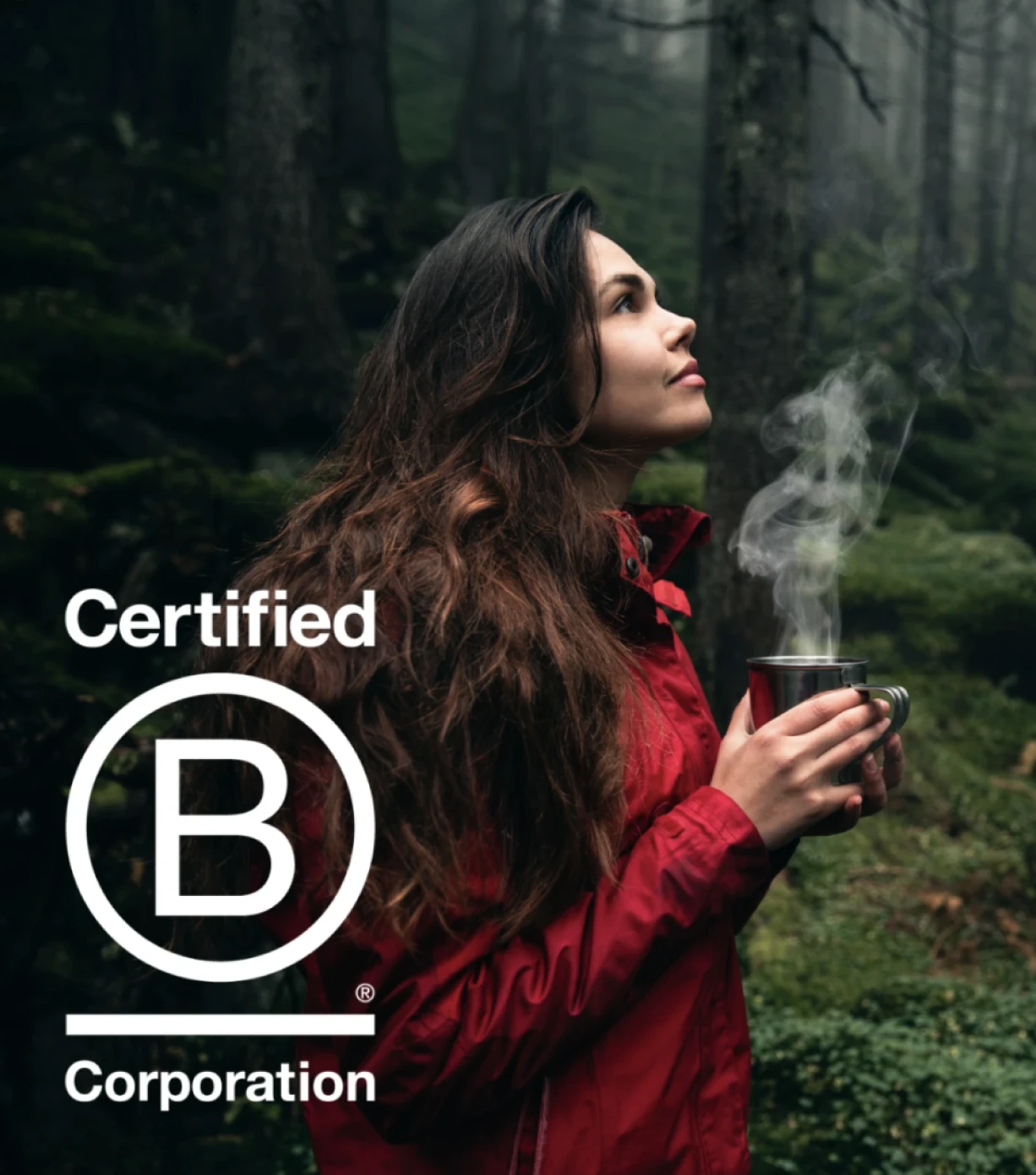 A woman traveler in a vibrant red jacket enjoys a hot drink from a cup amidst a serene mossy forest. A white B-Corp Certified logo is visible in the lower-left corner of the image.